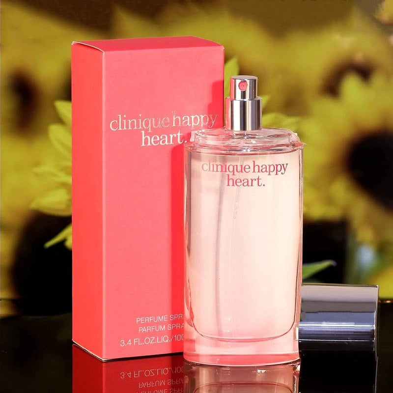 Clinique Happy Heart perfume bottle and packaging on a reflective surface with a blurred floral background