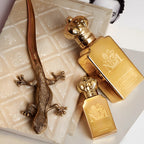 Two gold perfume bottles with a decorative lizard on a textured surface
