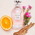 Coach Dreams perfume bottle with an orange, wooden piece, and flowers on a light background