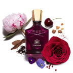 Creed Carmina perfume bottle surrounded by flowers and spices on a white background