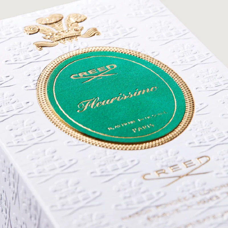 Close-up of a Creed perfume box with gold and green design on a white background