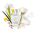 Creed perfume bottle surrounded by flowers and vanilla beans on a white background