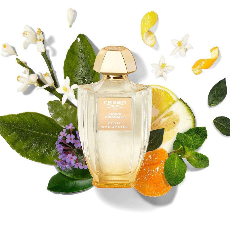 Creed perfume bottle surrounded by citrus fruits and flowers on a white background