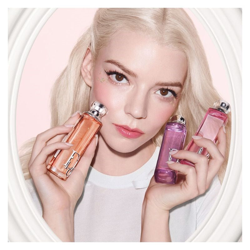 Woman holding three perfume bottles against a pink background