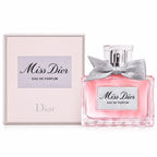 Dior Miss Dior Eau de Parfum bottle with a silver bow next to its light pink packaging box on a white background.