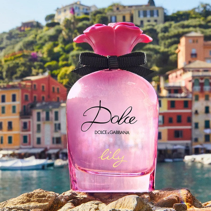 Pink Dolce & Gabbana perfume bottle with a scenic background of colorful buildings and water.