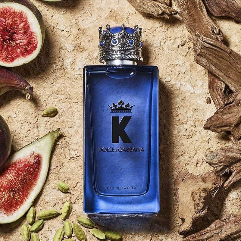 Blue Dolce & Gabbana perfume bottle with decorative cap on a textured surface with figs and cardamom pods.