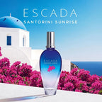 Escada Santorini Sunrise perfume bottle with a scenic background of pink flowers and a blue sky