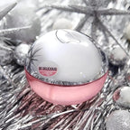 Pink and white perfume bottle with 'Be Delicious' label on a silver tinsel background