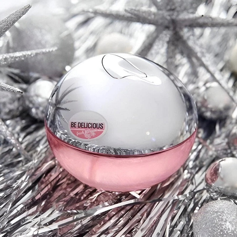 Pink and white perfume bottle with 'Be Delicious' label on a silver tinsel background