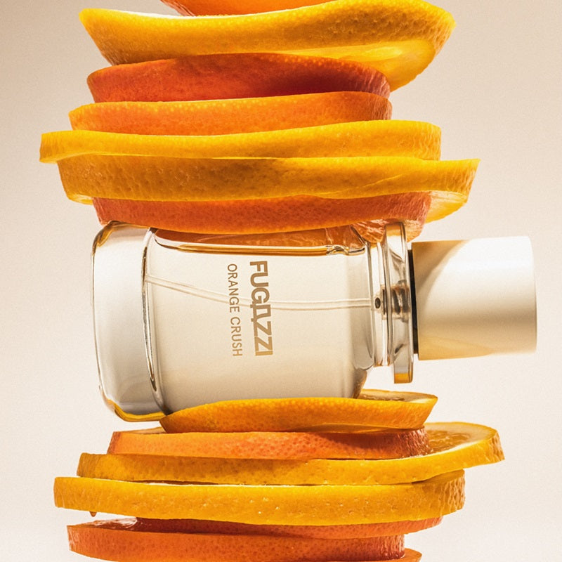 Fugazzi Orange Crush Eau de Parfum 100ml bottle lying on its side between stacked orange slices
