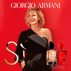 Giorgio Armani advertisement with a woman in a black dress and two perfume bottles on a red background.
