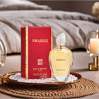 Givenchy Amarige perfume bottle and packaging on a decorative surface with a candle and glassware in the background.