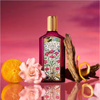 Gucci Flora perfume bottle with floral design on a reflective surface against a pink background