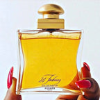 Hermes 24 Faubourg perfume bottle held by a hand with red nail polish on a white background