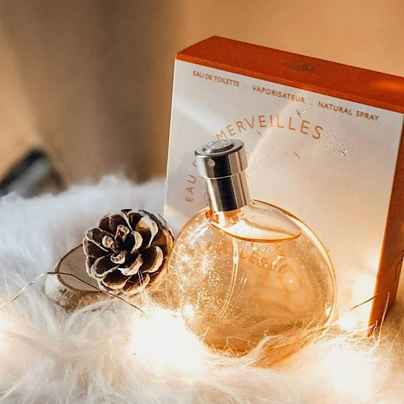 Perfume bottle with packaging on a fluffy surface with a pine cone.