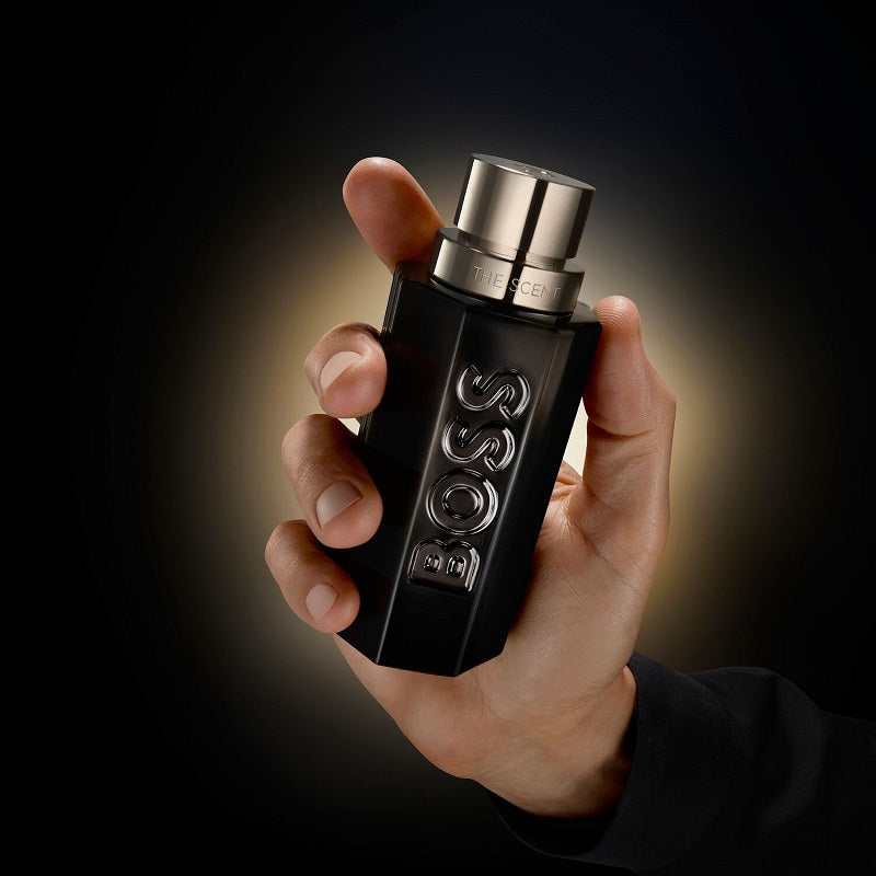 Hand holding a black Boss perfume bottle against a dark background