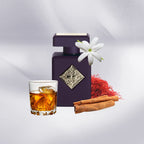 Purple perfume bottle with a glass of amber liquid, cinnamon sticks, and a white flower on a light gray background.