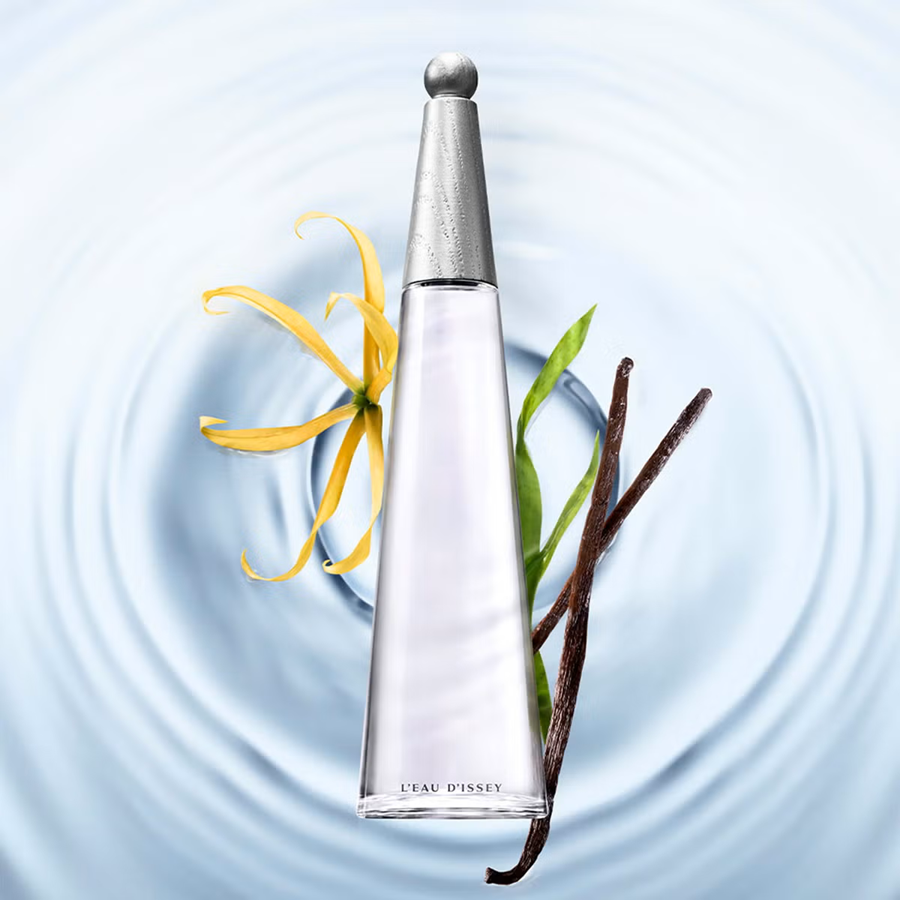 A clear glass perfume bottle with a silver cap, labeled 'L'EAU D'OPSI', centered over a light blue water ripple background. A yellow opal leaf and vanilla beans are placed around the bottle as styled props.