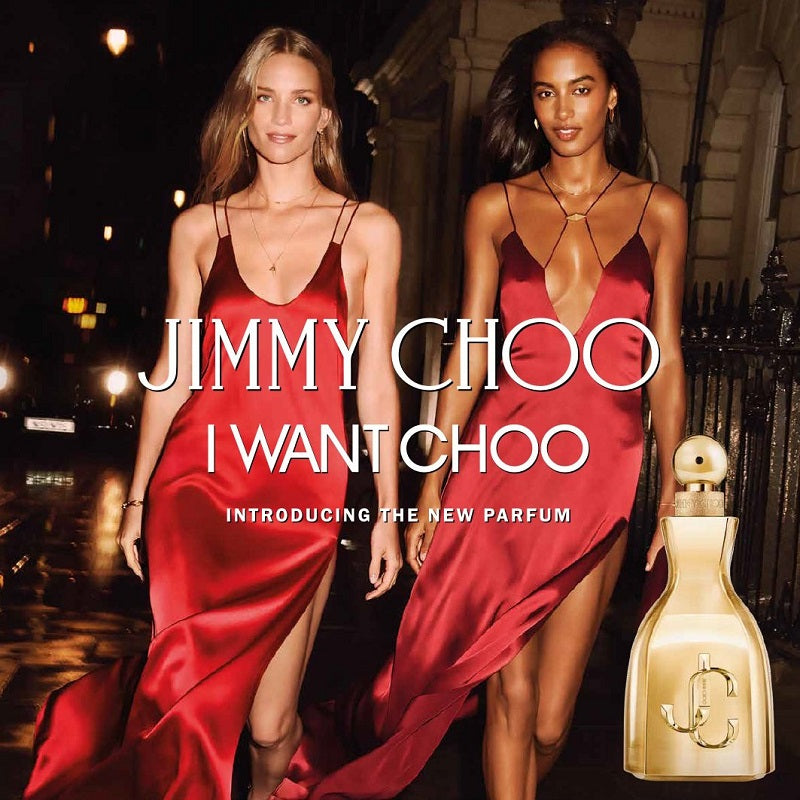 Two women in red dresses standing next to a gold perfume bottle with 'Jimmy Choo' branding.