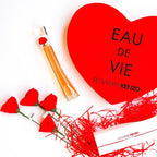 Perfume bottle with red heart-shaped box and flowers on a white background
