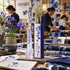 Kenzo Flower Ikebana Indigo bottle and box on a workshop table beside purple irises, sketchbooks and indigo-patterned textiles, with people working in the background