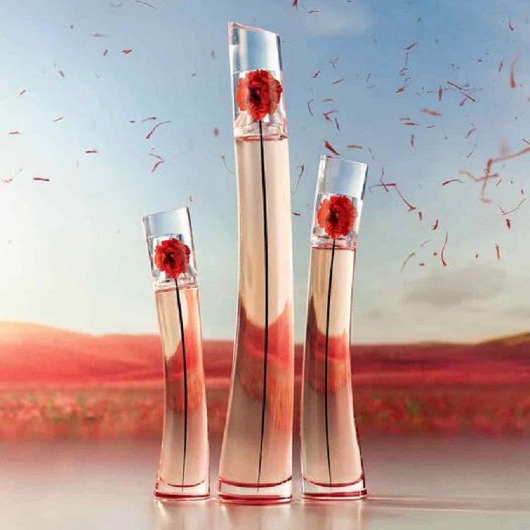 Three perfume bottles with red floral designs against a scenic background
