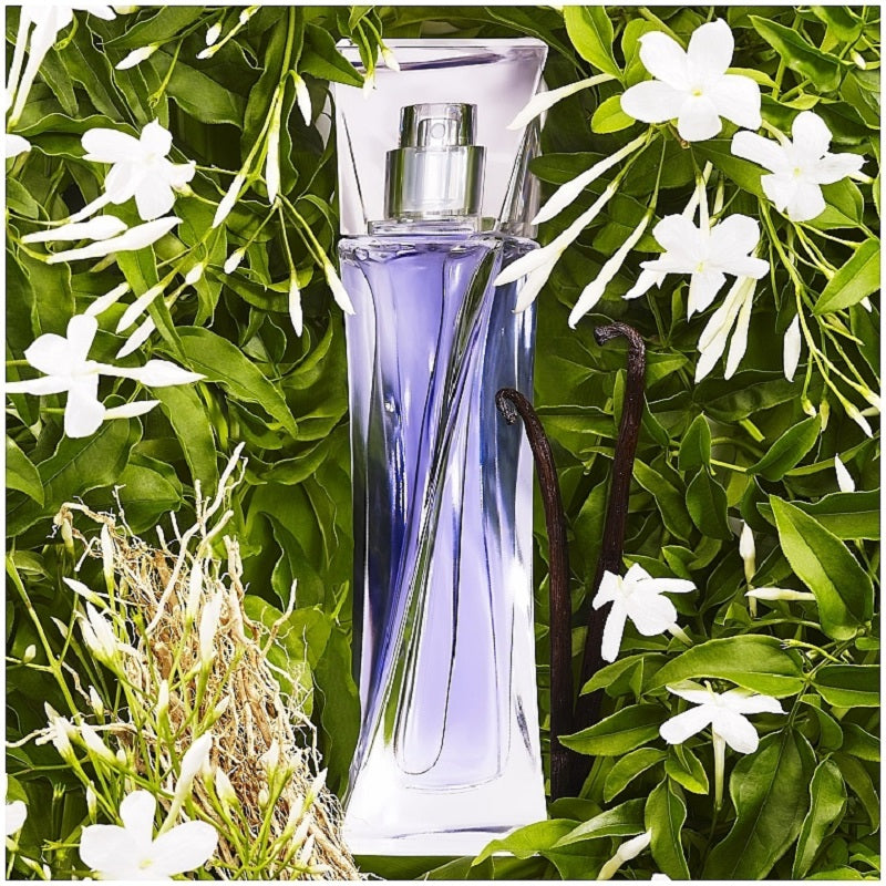 Perfume bottle with vanilla bean and flowers on a green leafy background