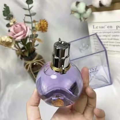 Hand holding a purple perfume bottle with a silver cap against a blurred background