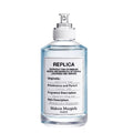 A transparent spray bottle of Maison Margiela Replica Sailing Day Eau de Toilette, with a white label and text.