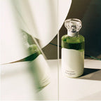 Green perfume bottle with a white label on a reflective surface