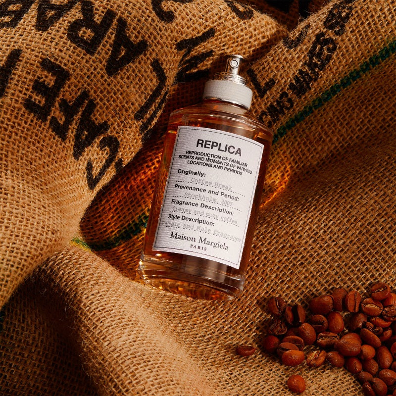Maison Margiela Replica perfume bottle laying on a bag of coffee bans.