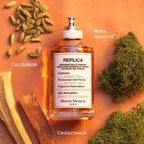 Perfume bottle labeled 'REPLICA' with cardamom, cedarwood, and moss on an orange background