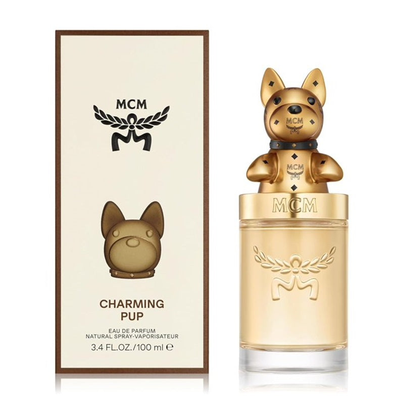 MCM Charming Pup Eau de Parfum bottle and packaging box. The bottle features a gold dog-shaped cap on a clear glass bottle filled with light amber liquid, next to its cream-colored box with brown borders and a black MCM logo.