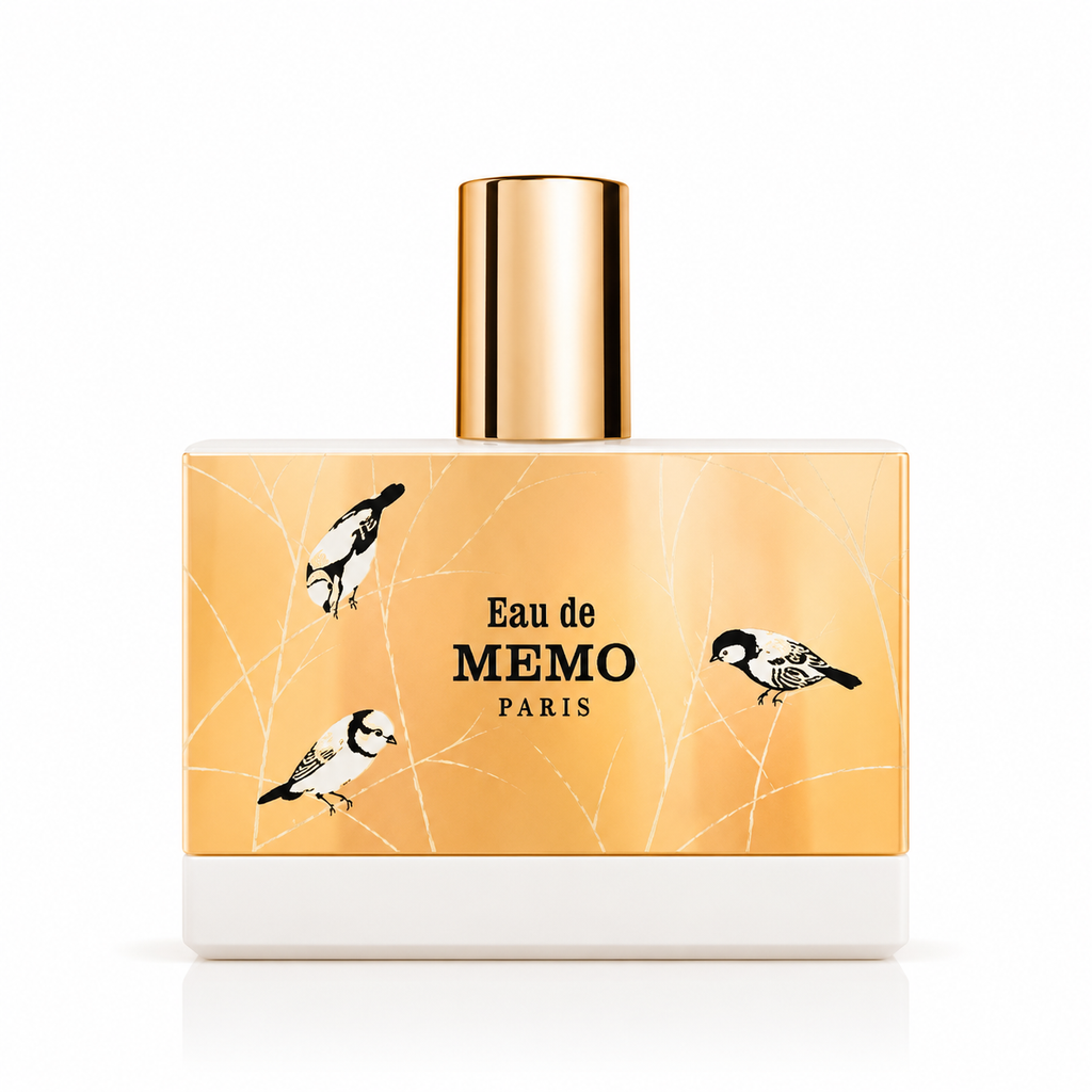 A rectangular perfume bottle with a metallic gold cap and a gold-toned label featuring black bird illustrations and the text 'Eau de MEMO PARIS'.