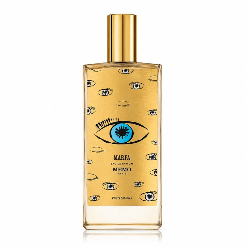 Memo Paris Marfa Eau de Parfum bottle with a gold cap and a gold body decorated with illustrated eyes, including a prominent blue and black eye in the center, on a white background.