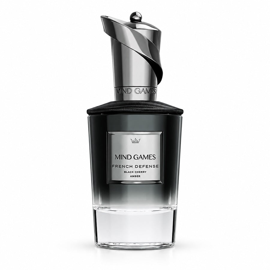 A bottle of Mind Games French Defense Black Cherry Amber perfume, featuring a dark gradient glass bottle with a metallic silver cap and a silver label on a white background.