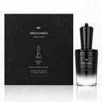 MIND GAMES Mentor White Fir Amber oud premium extrait de parfum, showing the black patterned retail box and the black-to-clear gradient perfume bottle on a white reflective surface.
