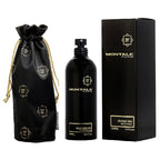 A black bottle of Montale Oud Edition Eau De Parfum with a spray dispenser, next to its black box adorned with white Montale branding and a gold design. A black fabric pouch with gold details is also displayed.