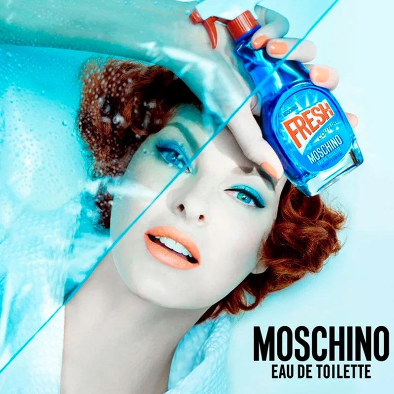 Model with blue makeup holding a Moschino Fresh Eau de Toilette bottle against a light blue background.
