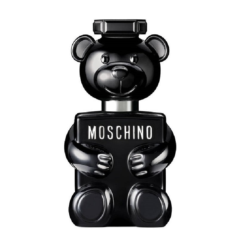 A bottle of Toy Boy Eau de Parfum by Moschino, featuring a black teddy bear shape with a smiling face and holding a sign with the brand name.