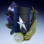 A*Men Rubber Flask Eau de Toilette by Mugler, featuring a black bottle with a metallic silver star on the front, presented with decorative plants and a slice of citrus.