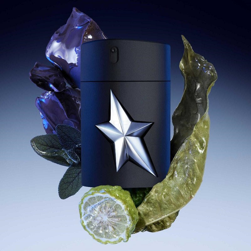 A*Men Rubber Flask Eau de Toilette by Mugler, featuring a black bottle with a metallic silver star on the front, presented with decorative plants and a slice of citrus.