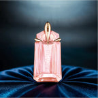 Pink perfume bottle with gold cap on a dark blue fabric background