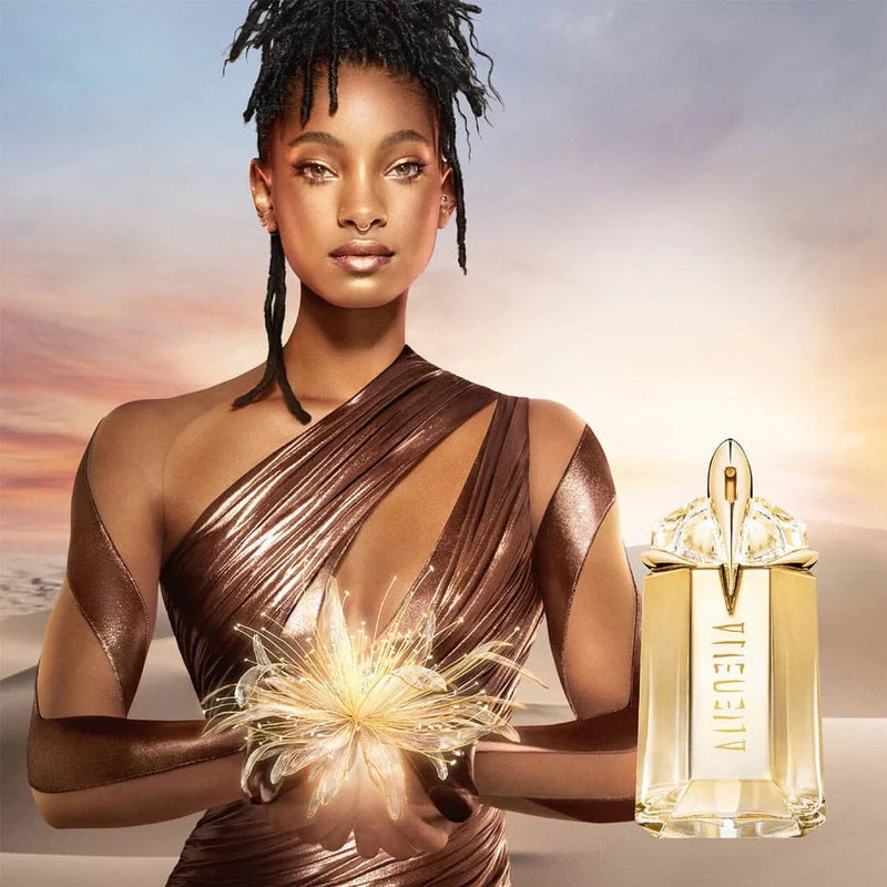 Woman holding a glowing flower with a gold perfume bottle labeled 'Viktor & Rolf Flowerbomb' against a sunset sky.
