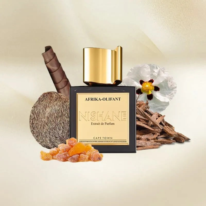 A perfume bottle labeled AFRIKA-OLIFANT NISHANE Extrait de Parfum by Cape Town, styled with a coconut, cinnamon stick, amber pieces, wood chips, and a flower on a warm cream background.