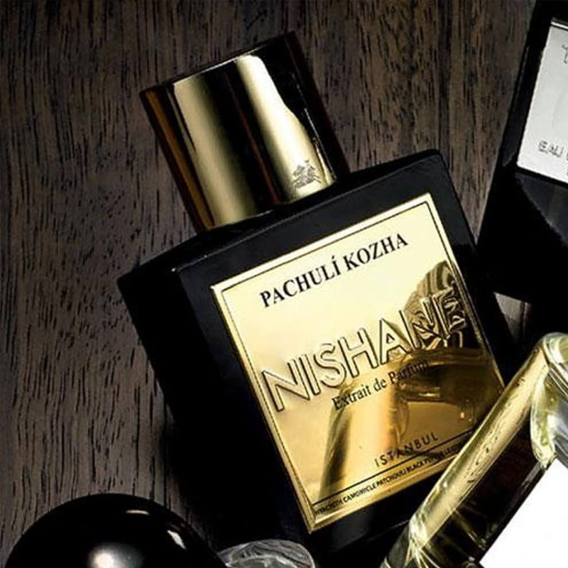 Pachuli Kozha Nishane Extrait de Parfum perfume bottle with a black body and a shiny gold label and cap, set on a dark wood background.