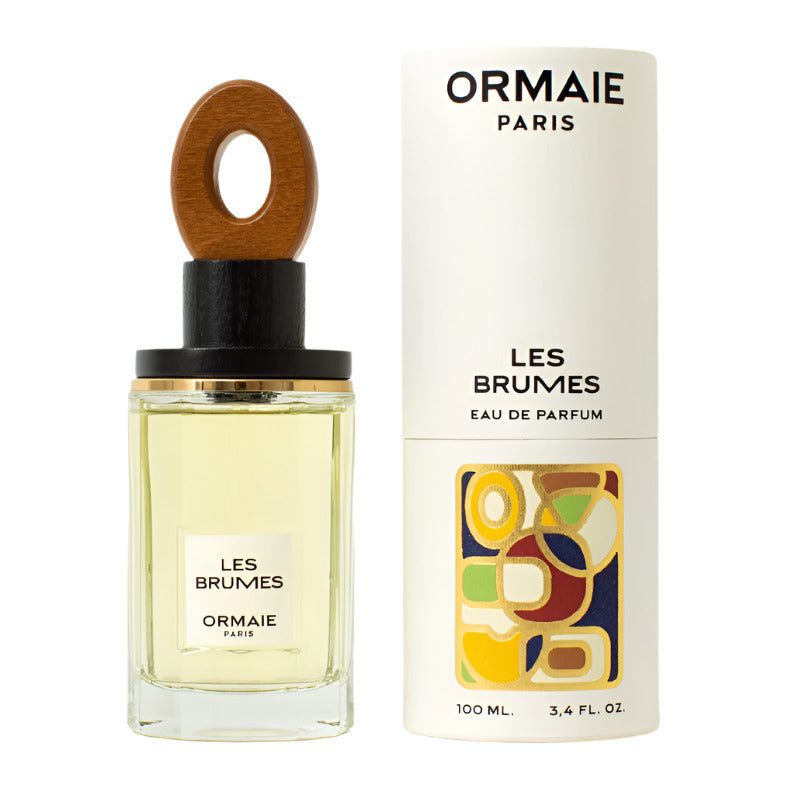 A bottle of Ormaie Les Brumes Eau de Parfum next to its packaging, which features a white background with colorful abstract shapes and the text 'LES BRUMES EAU DE PARFUM 100 ML'.