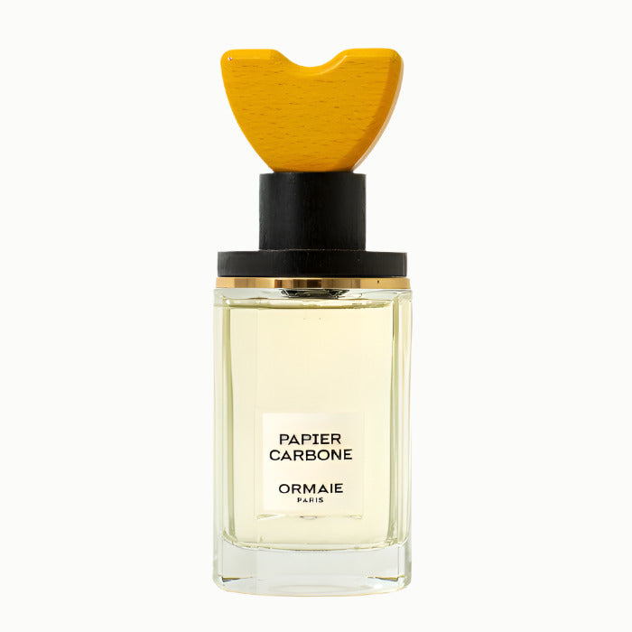 A bottle of Ormaie Papier Carbone eau de parfum with a yellow cap and a label that reads 'PAPIER CARBONE'.