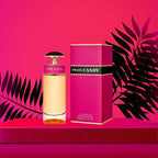 Prada Candy perfume bottle and packaging on a pink background with black leaves.